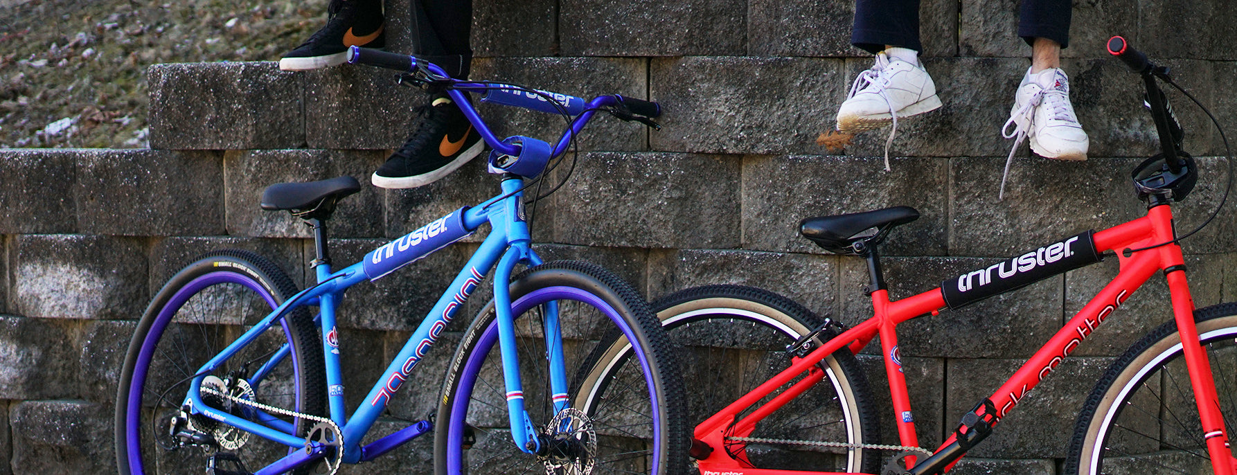 Two people sit on a wall with blue and red discount bikes parked below against stone steps outdoors.