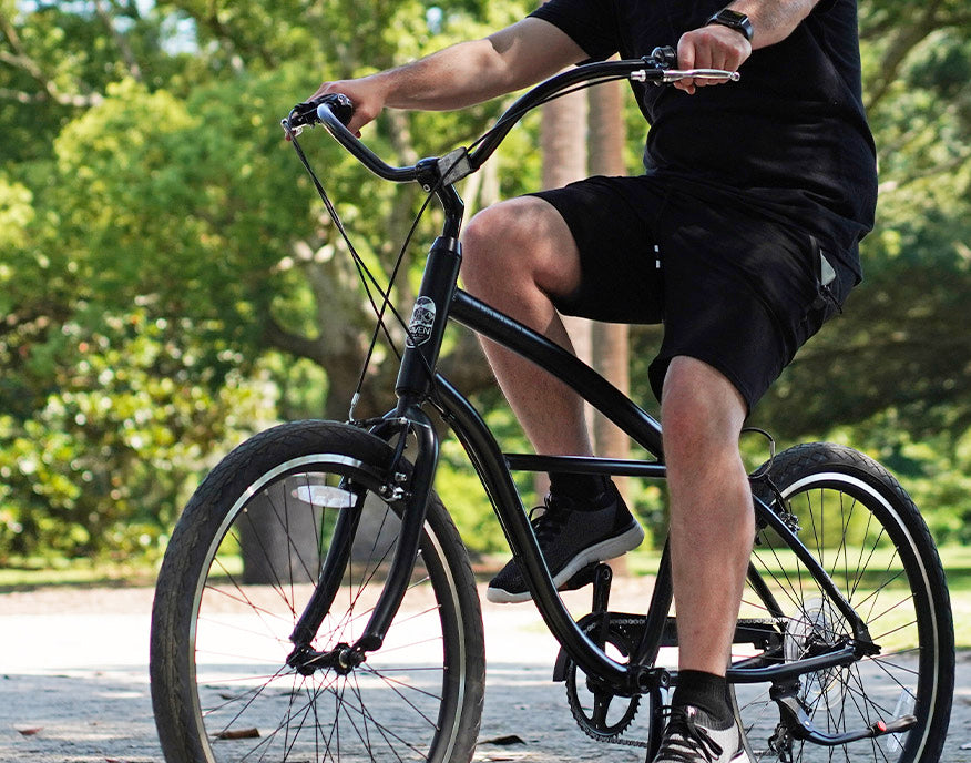 A man in black outfit riding a discount bicycle outdoors on a sunny day with green trees around.
