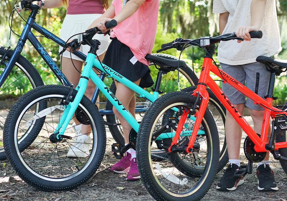 Children with discount bikes outdoors, standing beside blue and red bicycles in a park setting.