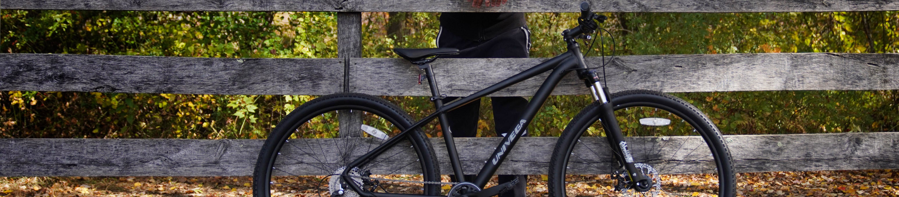 Black Univaga bicycle resting against a wooden fence in an outdoor setting during fall.